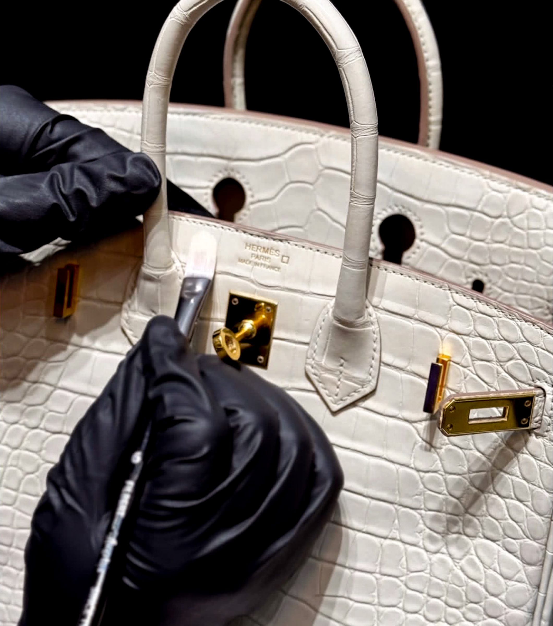 Colour being applied by hand to a white alligator bag with gold hardware