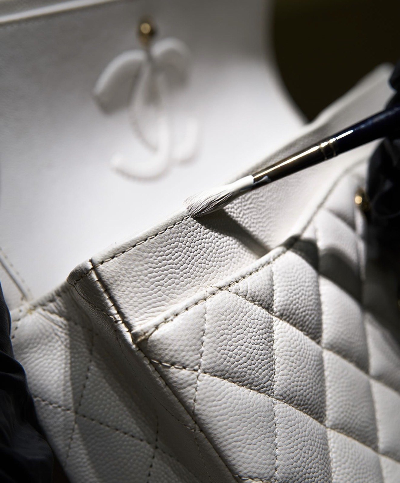 Colour being worked into the edge of a white caviar leather bag with a fine brush